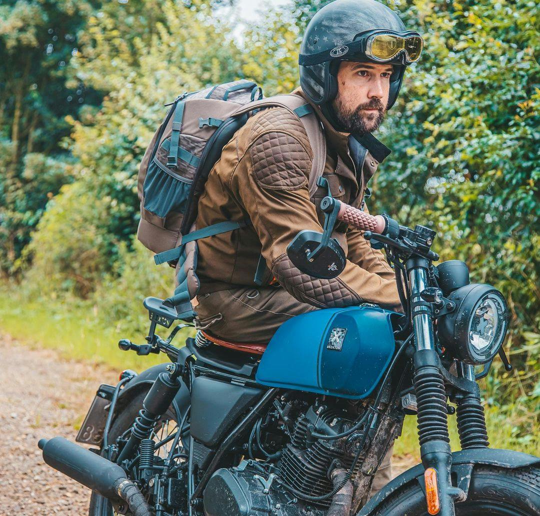 Rider of the Month Kev sitting sideways on his Brixton Rayburn 125 in Royal Blue Matt / Horizon Blue Matt on a forest road surrounded by green foliage
