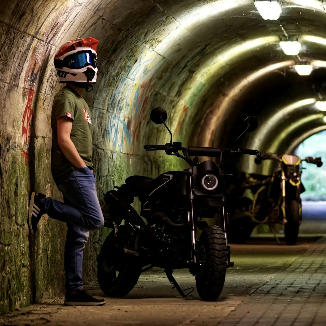 Rider of the Month Marco wearing his motorcycle helmet and googles while standing next to his Brixton Crossfire 125 XS in Backstage Black in a pedestrian tunnel