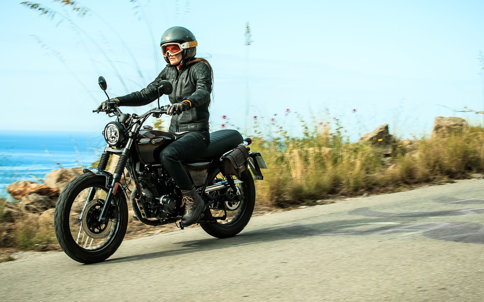 Landscape photo of a female Rider on a Brixton Cromwell 125 in Charly Brown riding on a coastal road