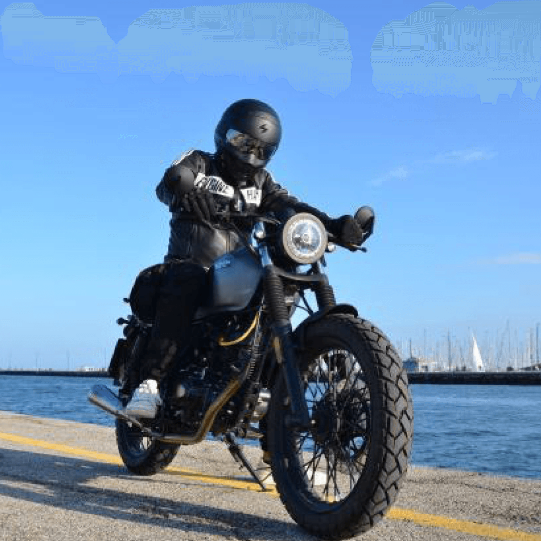 Rider of the Month Chris sitting on his Brixton Felsberg 125 in Timbewolf Grey at the pier with sailing boats and water in the back