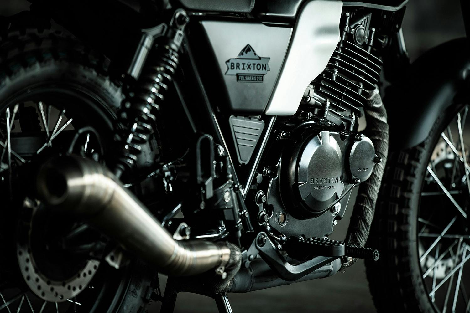 Cropped close-up of the motor, exhaust, footrest and logo detail on the right side of a Brixton Motorcycles 250 in Timberwolf Grey