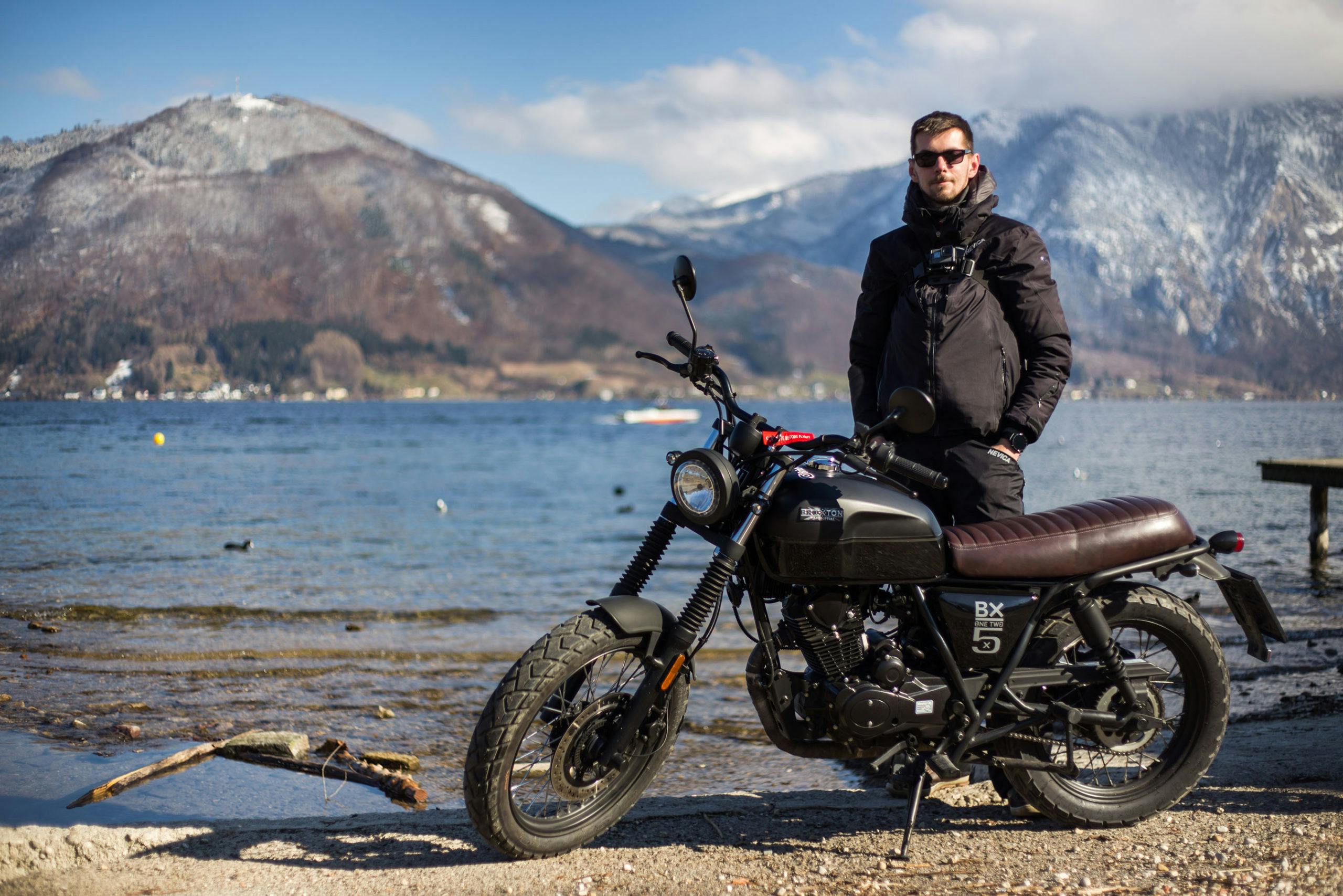 Rider of the Month: Robert next to his Brixton Cromwell 125 in Backstage Black standing next to the sea surrounded by mountains