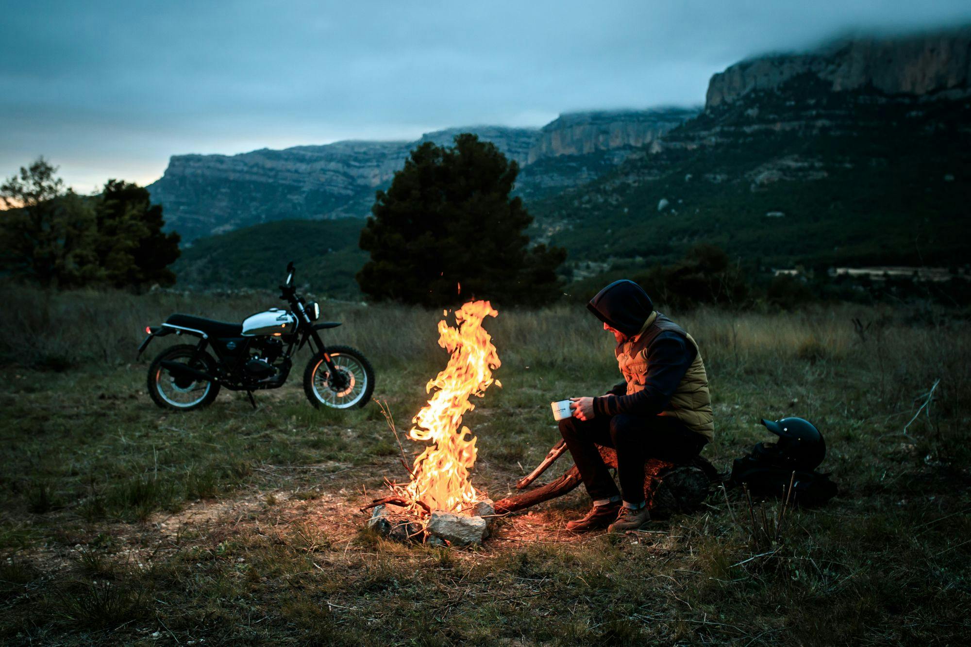 Brixton Felsberg 125 XC parked on a meadow with the rider sitting next to a campfire