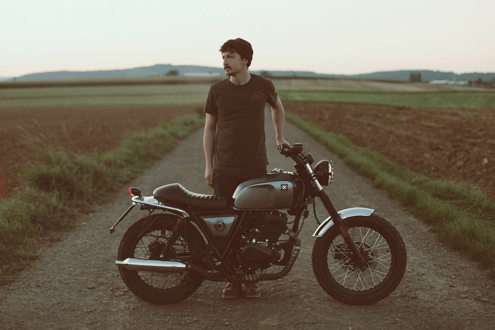 Rider of the Month Sidney with his Brixton Cromwell 125 in Timberwolf Grey standing on a field road